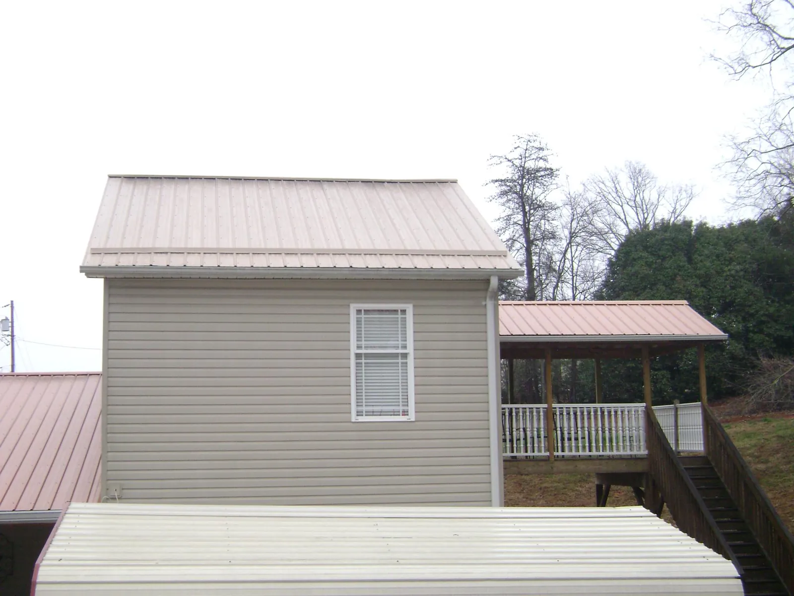 Tan metal roofs on a two story addition and attached porch, from a Roof Replacement job in Decatur